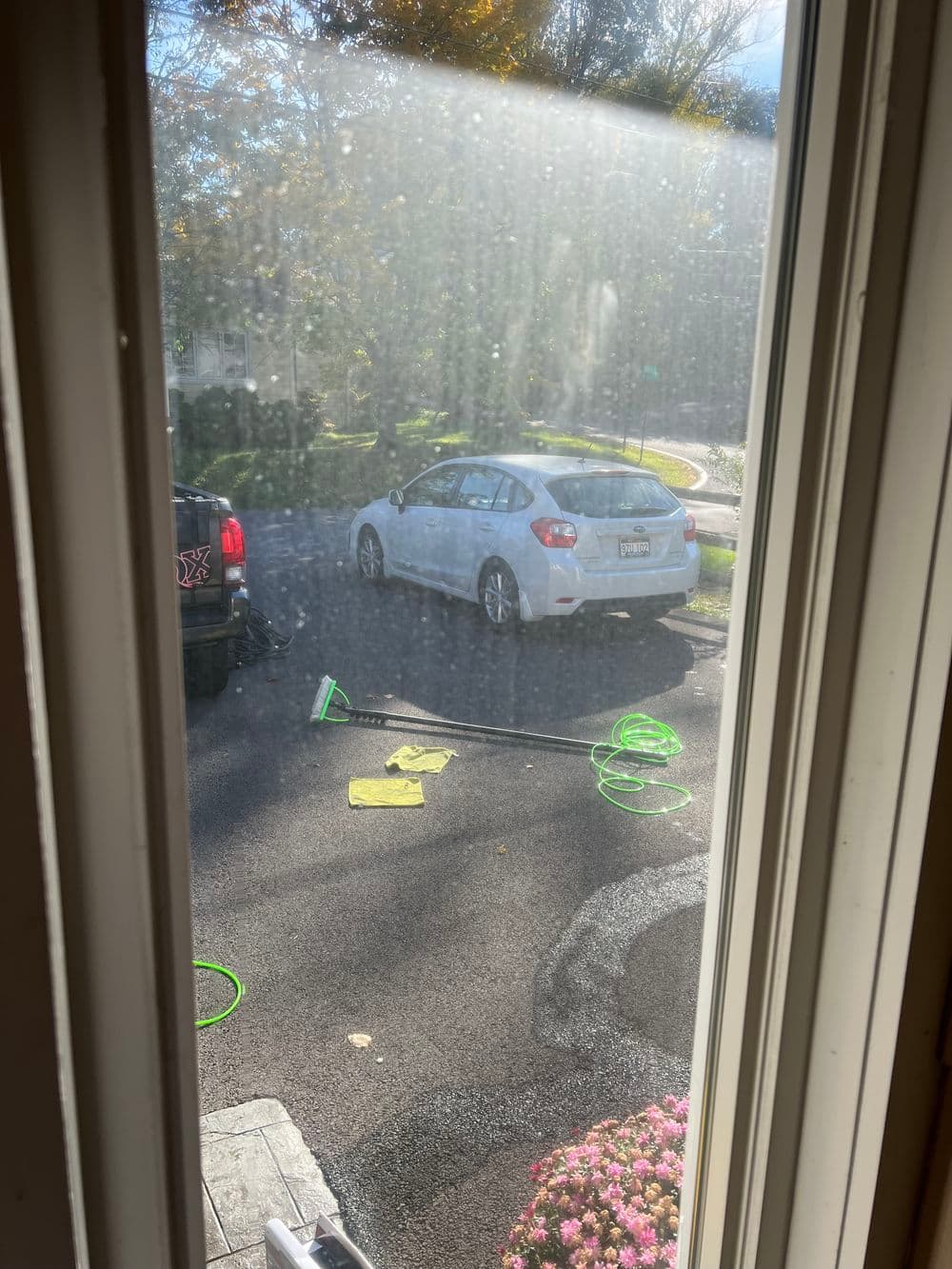 View from a window showing a white car parked outside with cleaning tools on the ground.